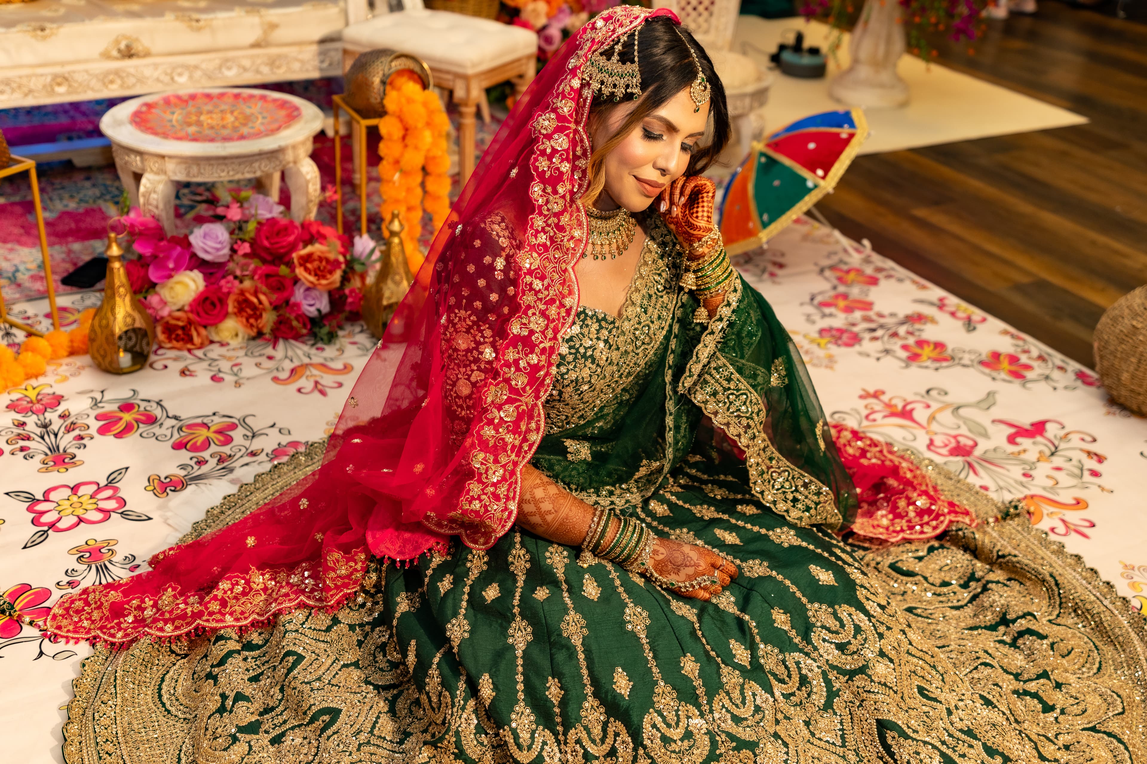 Seated bridal portrait surrounded by richly coloured Mehendi decor.
