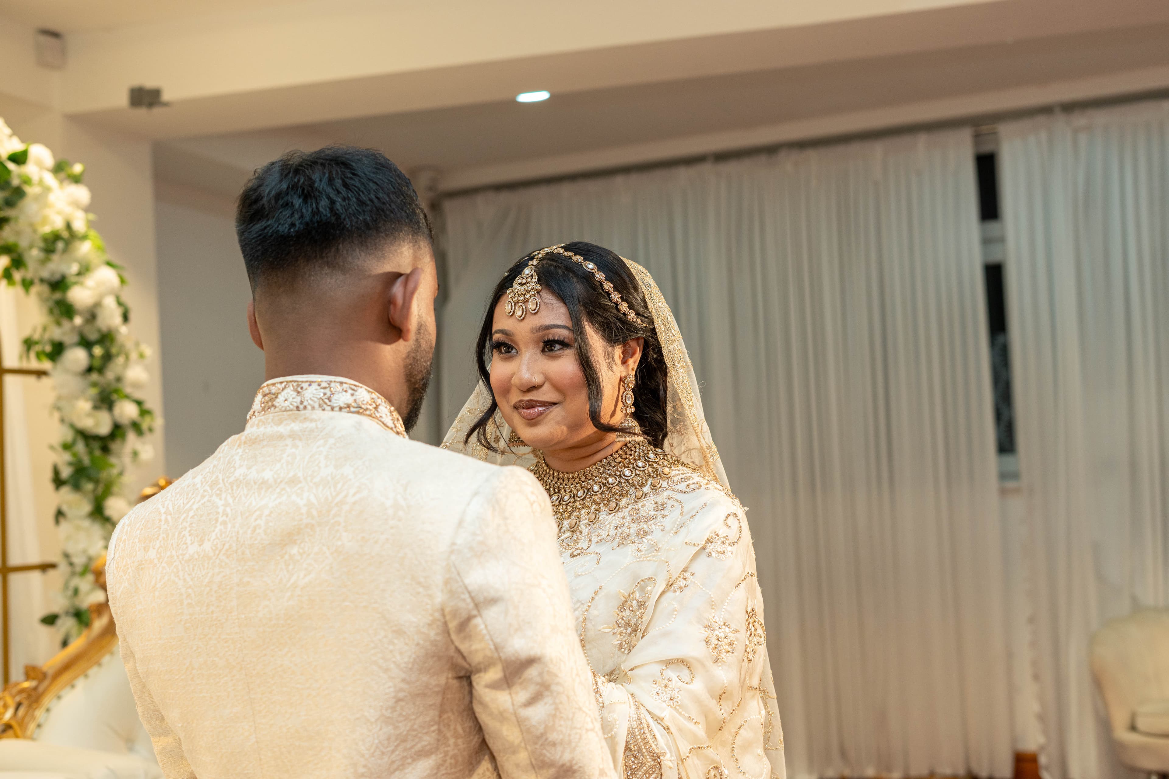 Couple facing one another on a white-and-gold wedding stage.