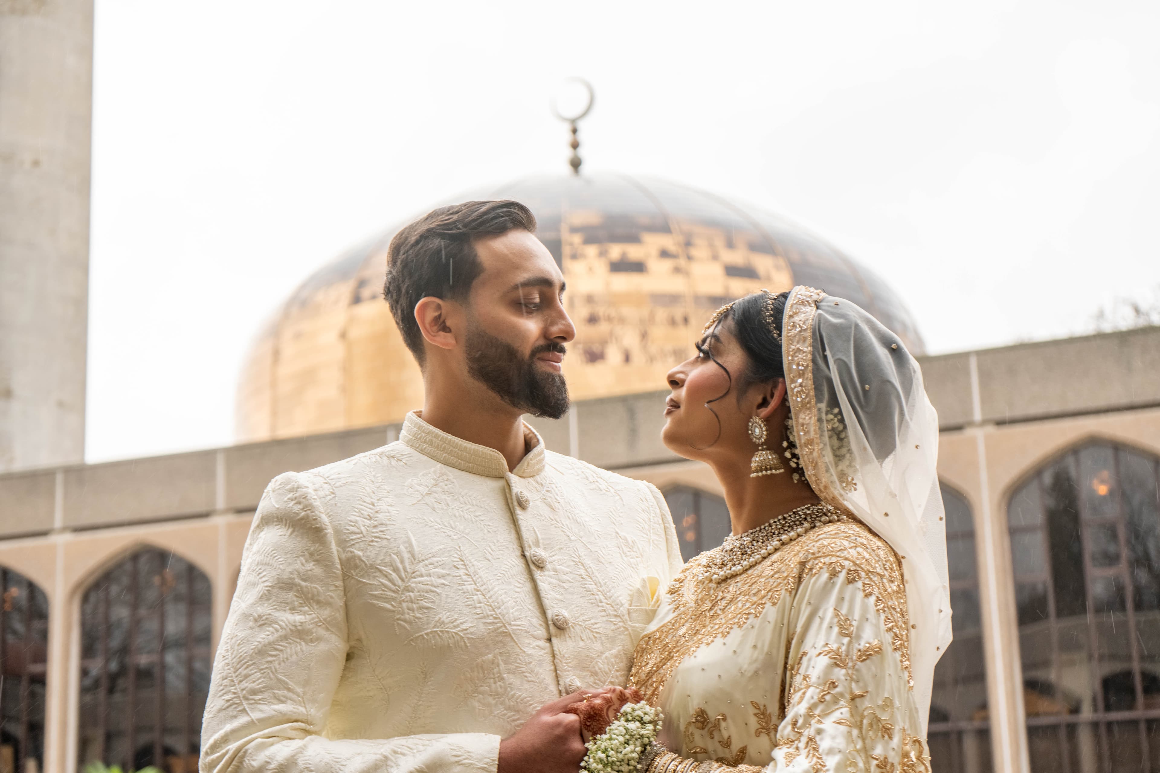 Couple photographed outside a mosque beneath a large dome.