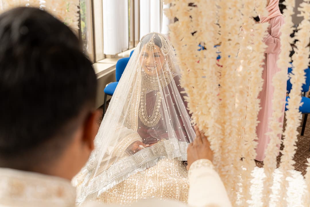 Bride smiling towards the groom during a wedding ceremony beneath floral decor.